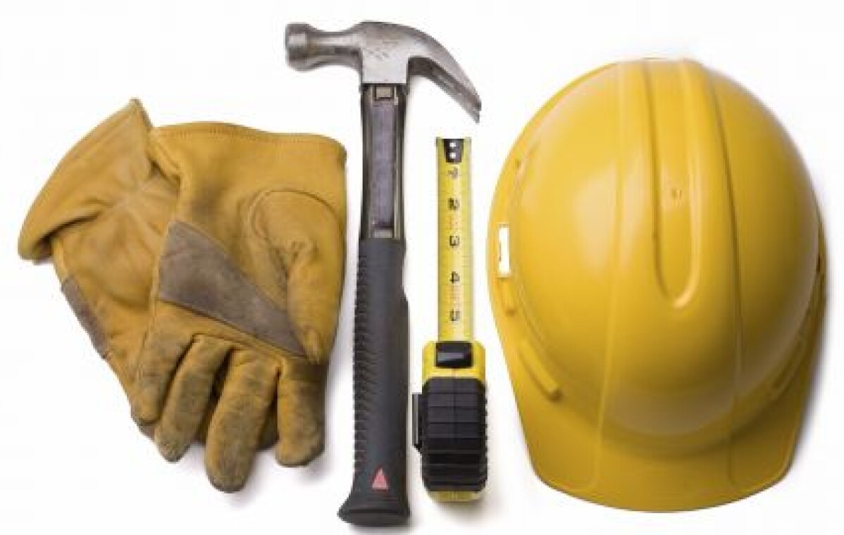 Casque de chantier jaune, gants de travail, marteau et mètre ruban posés côte à côte