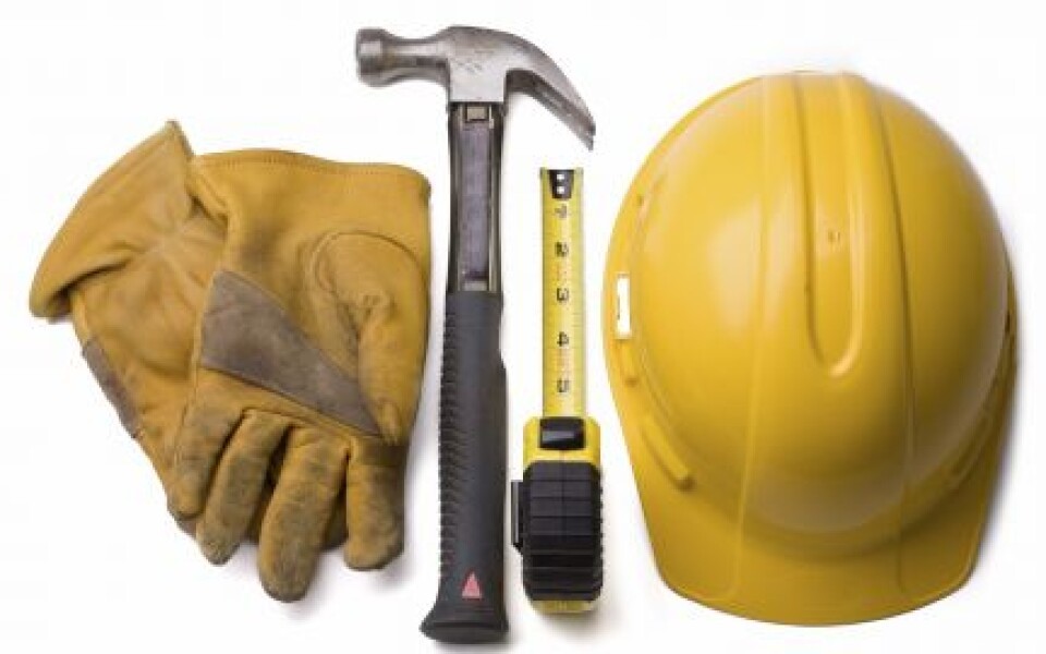 Casque de chantier jaune, gants de travail, marteau et mètre ruban posés côte à côte