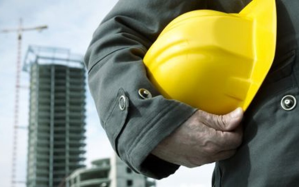 Chef de chantier tenant un casque jaune devant un immeuble en construction et une grue