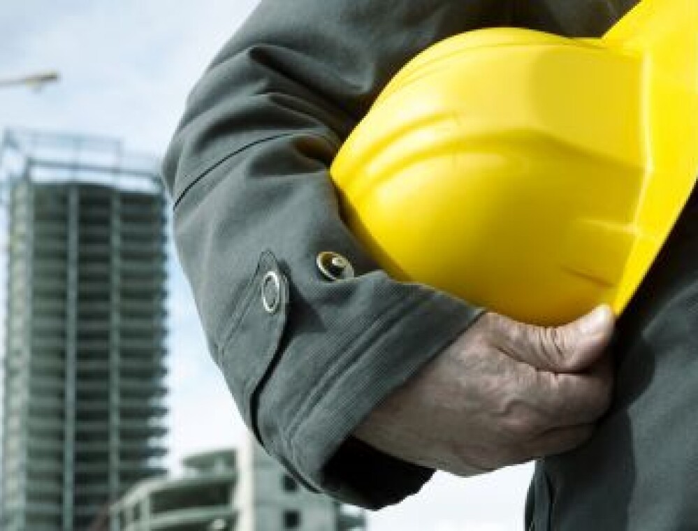 Chef de chantier tenant un casque jaune devant un immeuble en construction et une grue